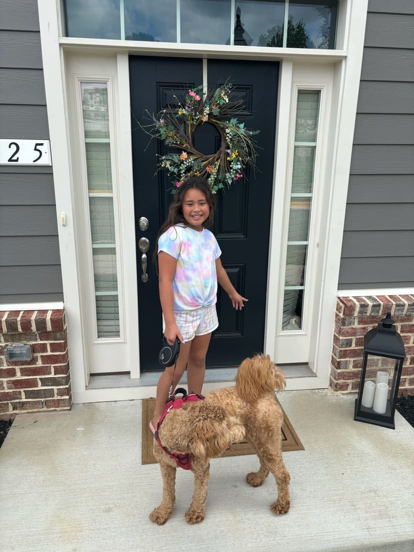 Girl standing by a black front door with a dog, colorful floral wreath above the entrance.
