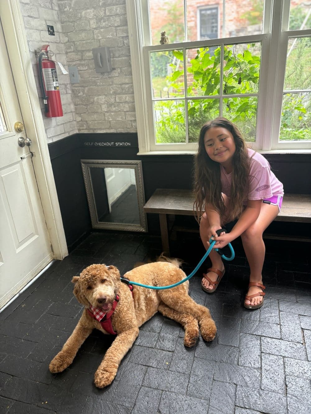 Girl sitting with a brown dog on a leash in a cozy, well-lit indoor space.